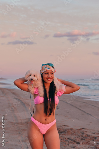 Happy young woman in bikini carrying her cute furry puppy on her shoulders at the seashore