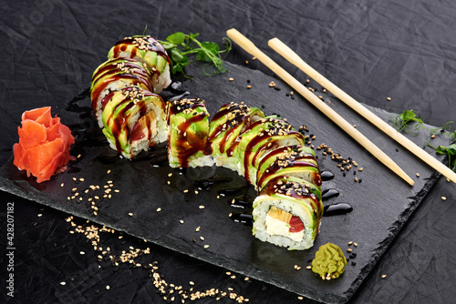 Roll sushi with avocado and fish on a black stone substrate and a dark background