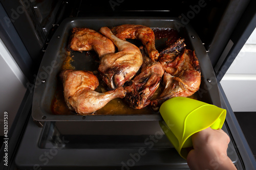hand taking chicken out of the oven in the kitchen. Concept homemade food.