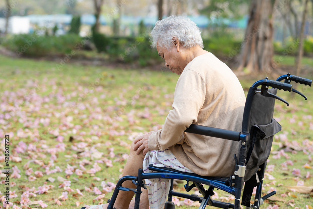 Fototapeta premium Asian senior or elderly old lady woman patient pain her knee on wheelchair in park, healthy strong medical concept.