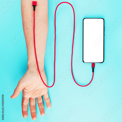 The hand is connected by a red power cord to a smartphone with free space on a blue background. photo