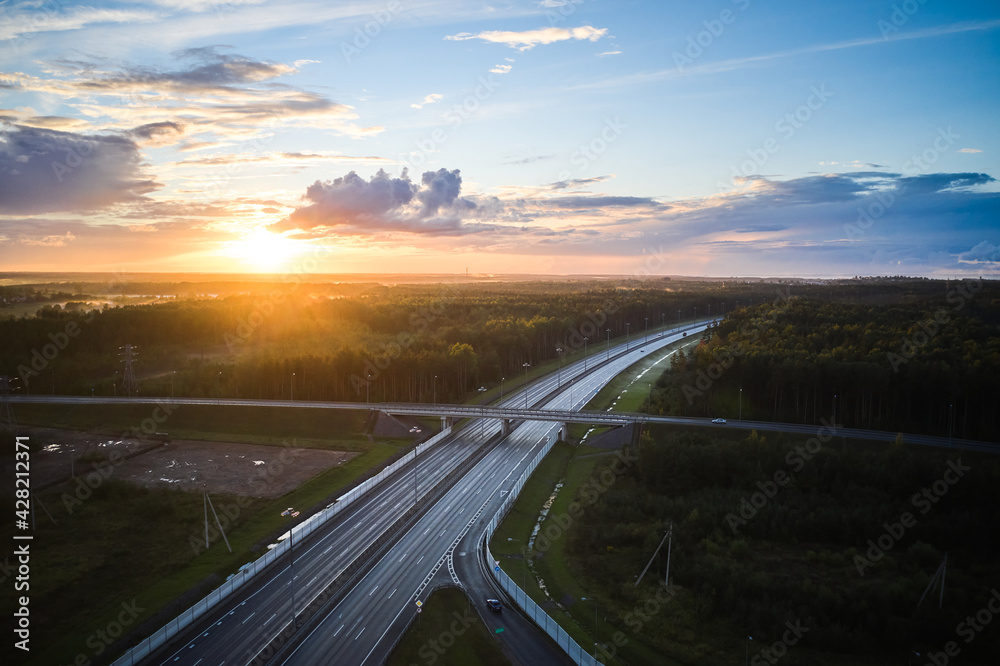 Aerial view of the sunset over highway and green forest in dusk
