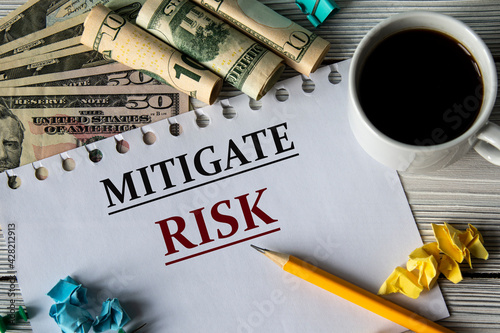 MITIGATE RISK - words on a white sheet against a background of banknotes, cups of coffee and pencil photo