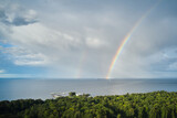 Aerial view of rainbow over sea and forest on a coastline