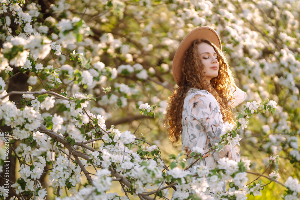 Curly woman with the hat posing in blooming spring park. The concept of relax, travel, paradise, romance and spring vacation. Fashion style. Curly woman with the hat posing in blooming spring park. The concept of relax, travel, paradise, romance and spring vacation. Fashion style.
