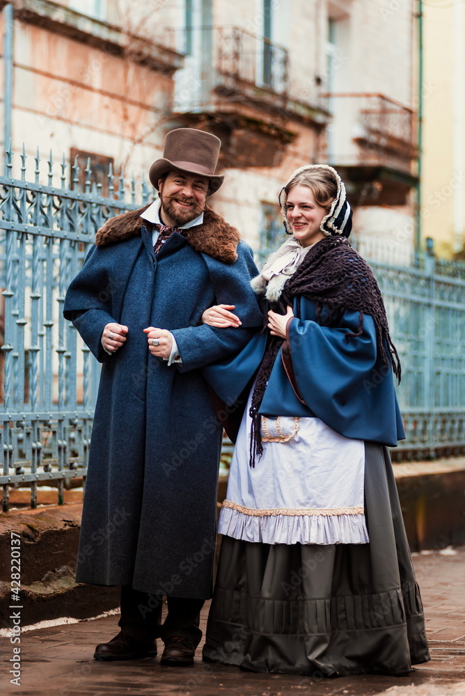 A man and a woman, elegantly dressed, in 19th-century clothes, walk and talk