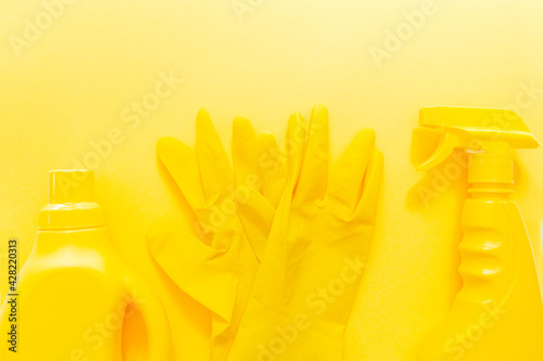 Yellow onochrome flat lay of cleaning tools. Colorful rubber gloves, spray, gel bottle