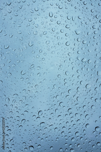 Wet windshield, taken from inside the car.Rain falls on the surface of a car glass window with a gray background. Natural patterns of raindrops on the windshield. Water drops wallpaper.