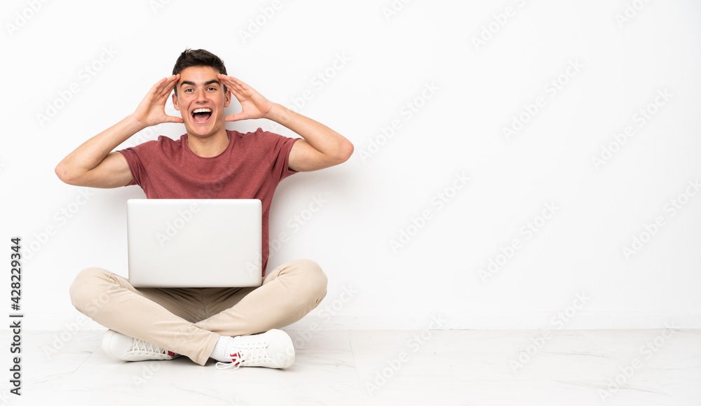 Teenager man sitting on the flor with his laptop with surprise expression Teenager man sitting on the flor with his laptop with surprise expression