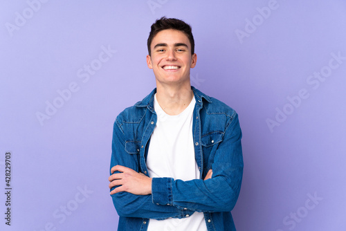 Teenager caucasian  handsome man isolated on purple background keeping the arms crossed in frontal position photo