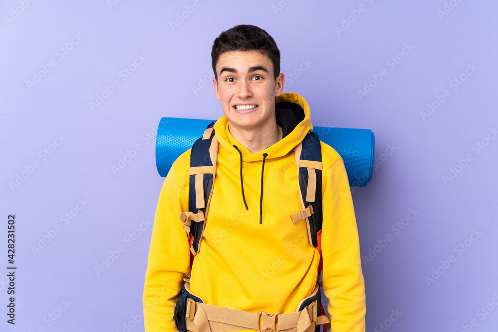 Teenager caucasian mountaineer man with a big backpack isolated on purple background having doubts and with confuse face expression Teenager caucasian mountaineer man with a big backpack isolated on purple background having doubts and with confuse face expression
