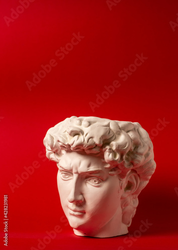 Gypsum statue of David's head. Michelangelo's David statue plaster copy isolated on red background. Ancient greek sculpture, statue of hero.