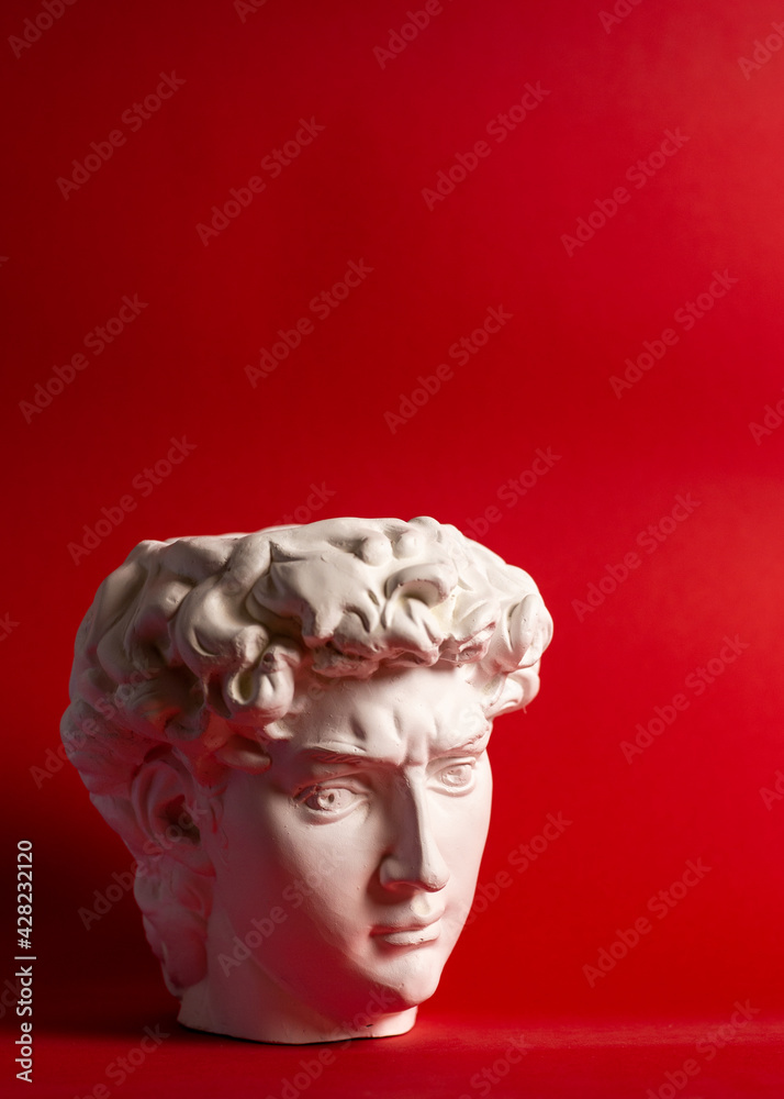 Gypsum statue of David's head. Michelangelo's David statue plaster copy isolated on red background. Ancient greek sculpture, statue of hero. Gypsum statue of David's head. Michelangelo's David statue plaster copy isolated on red background. Ancient greek sculpture, statue of hero.
