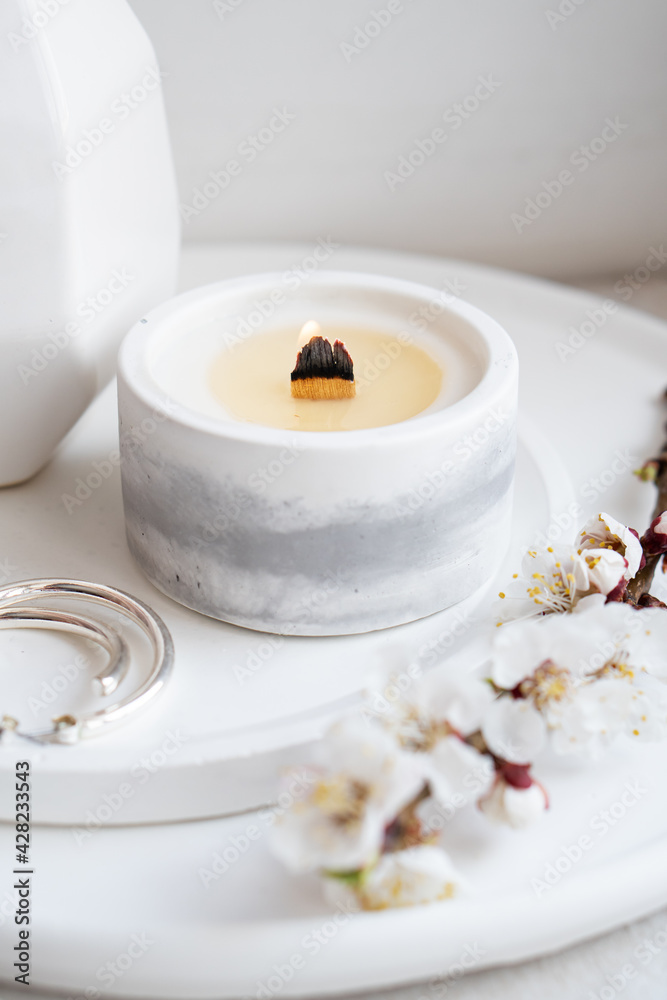Blooming apricot tree branches in vase and burning candle on round tray in home interior Blooming apricot tree branches in vase and burning candle on round tray in home interior