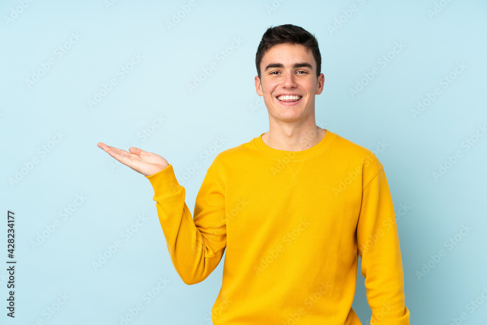 Teenager caucasian handsome man isolated on purple background holding copyspace imaginary on the palm to insert an ad Teenager caucasian handsome man isolated on purple background holding copyspace imaginary on the palm to insert an ad