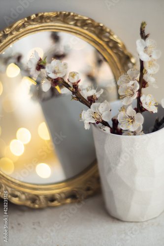 Blooming apricot tree branches in cup and burning candle in front of mirror © Daria Minaeva