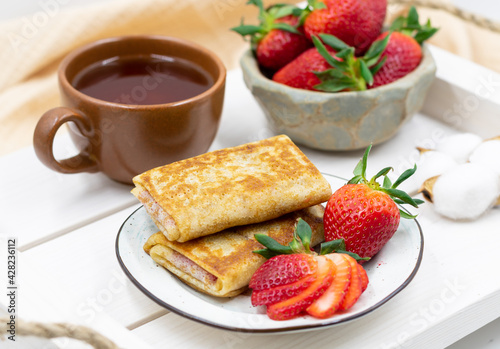 Pancakes with strawberry filling. Served with tea and ripe strawberries. Shot in a high key.
