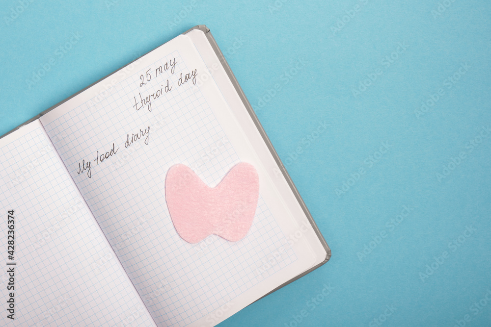 notepad and silhouette of the thyroid gland cut out of pink felt on a blue background, nutrition for diseases of the thyroid gland concept notepad and silhouette of the thyroid gland cut out of pink felt on a blue background, nutrition for diseases of the thyroid gland concept