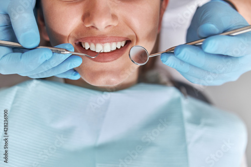 Cheerful positive dentist and client in dentistry. Female patient at dental procedure  doctor using dental instruments in modern dental clinic  close up.