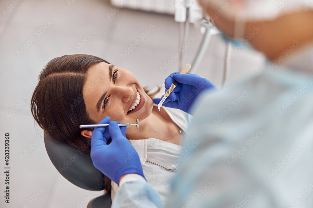 Portrait of young dentist in gloves examining teeth of female client in the hospital Portrait of young dentist in gloves examining teeth of female client in the hospital