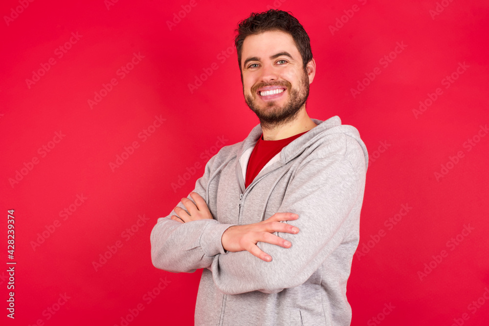 Young caucasian man wearing tracksuit over red background happy face smiling with crossed arms looking at the camera. Positive person.