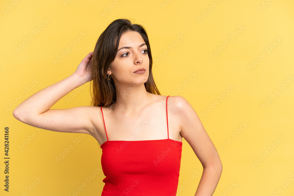 Young caucasian woman isolated on yellow background having doubts while scratching head Young caucasian woman isolated on yellow background having doubts while scratching head