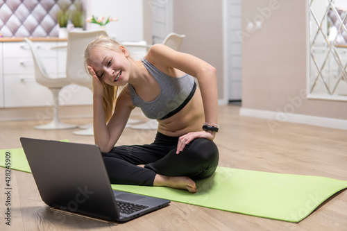young attractive girl resting after fitness at home and looking at the laptop. quarantine fitness concept. High Quality