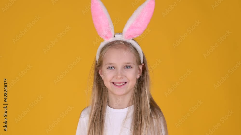 Little girl with rabbit ears on her head is having fun isolated on yellow studio background. smiles cheerfully. Spring holiday concept Little girl with rabbit ears on her head is having fun isolated on yellow studio background. smiles cheerfully. Spring holiday concept