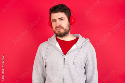 Displeased Young caucasian man wearing tracksuit over red background frowns face feels unhappy has some problems. Negative emotions and feelings concept