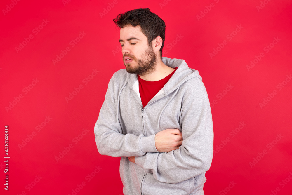 Young caucasian man wearing tracksuit over red background got stomachache Young caucasian man wearing tracksuit over red background got stomachache