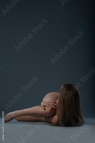 Studio photo of a young naked woman lying down on the floor and touching herself