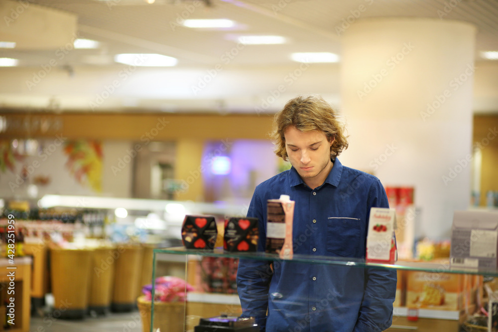 Fototapeta premium Young man shopping in supermarket, reading product information