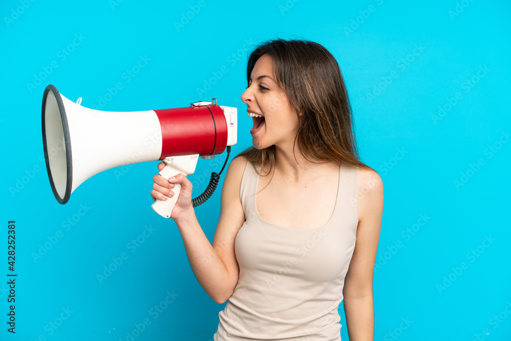 Young caucasian woman isolated on blue background shouting through a megaphone to announce something in lateral position Young caucasian woman isolated on blue background shouting through a megaphone to announce something in lateral position
