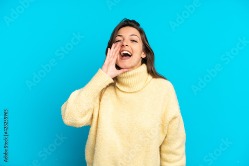 Young caucasian woman isolated on blue background shouting with mouth wide open © luismolinero
