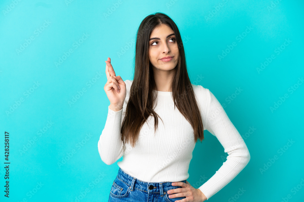 Young caucasian woman isolated on blue background with fingers crossing and wishing the best Young caucasian woman isolated on blue background with fingers crossing and wishing the best