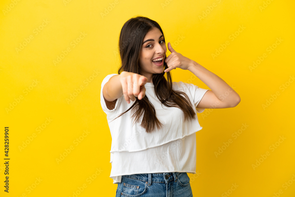 Young caucasian woman isolated on yellow background making phone gesture and pointing front Young caucasian woman isolated on yellow background making phone gesture and pointing front