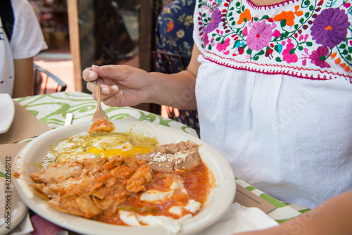 Latin Mexican woman weraing a Mexican traditional embroidered blouse, having chilaquiles with eggs and beans with spicy salsa for breakfast in the city of Ensenada Baja California.