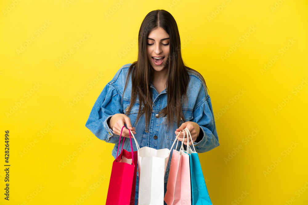 Young caucasian woman isolated on blue background holding shopping bags and looking inside it