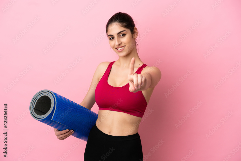 Young sport caucasian woman going to yoga classes while holding a mat showing and lifting a finger Young sport caucasian woman going to yoga classes while holding a mat showing and lifting a finger