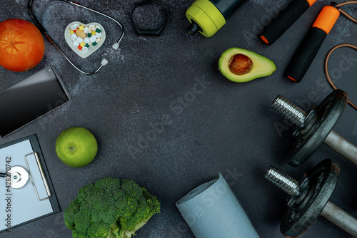 Healthy lifestyle powerlifting workout concept with grip cast iron dumbbell, smartphone, avocados, broccoli, apple on a cement floor. Empty copy space photo