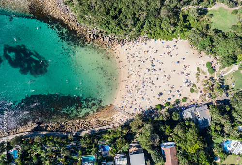Panoramic aerial bird's eye view of Shelly Beach at the southeastern end of Manly, a beachside suburb of Sydney, New South Wales, Australia. Hot summer day with many people on the beach enjoying sun.