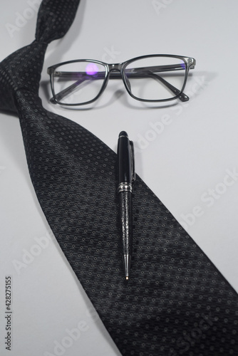 Selective Focus Of A Black Necktie, Black Elegant Ball Pen and Black Spectacle Isolated With White Background