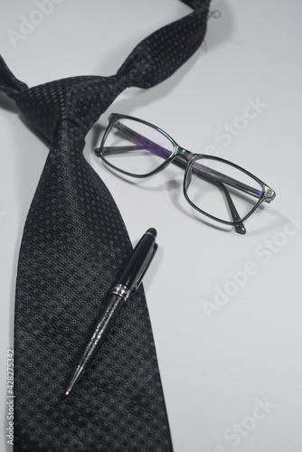 Selective Focus Of A Black Necktie, Black Elegant Ball Pen and Black Spectacle Isolated With White Background