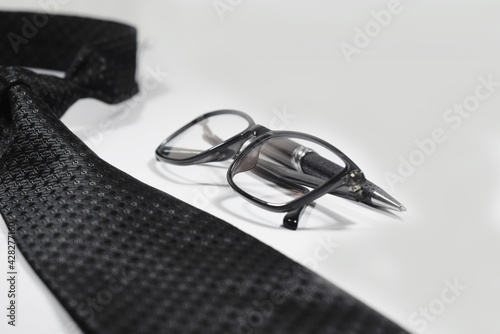 Selective Focus Of A Black Necktie, Black Elegant Ball Pen and Black Spectacle Isolated With White Background