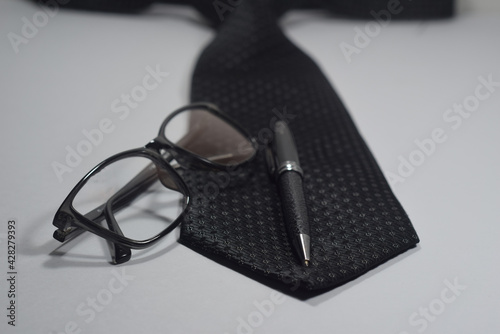 Selective Focus Of A Black Necktie, Black Elegant Ball Pen and Black Spectacle Isolated With White Background