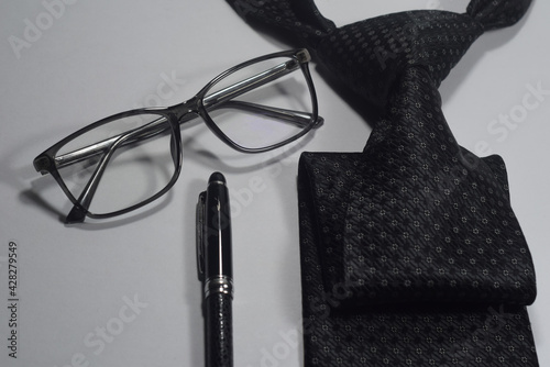 Selective Focus Of A Black Necktie, Black Elegant Ball Pen and Black Spectacle Isolated With White Background