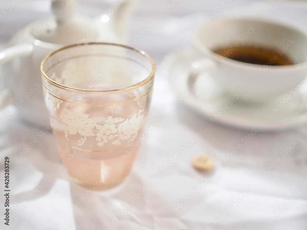 Pretty pink glass with tea and teapot on a white background Pretty pink glass with tea and teapot on a white background