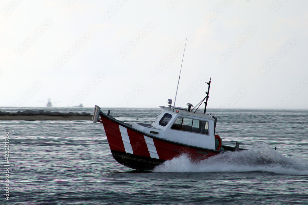 Fototapeta premium Red and white boat moving toward shore during overcast weather