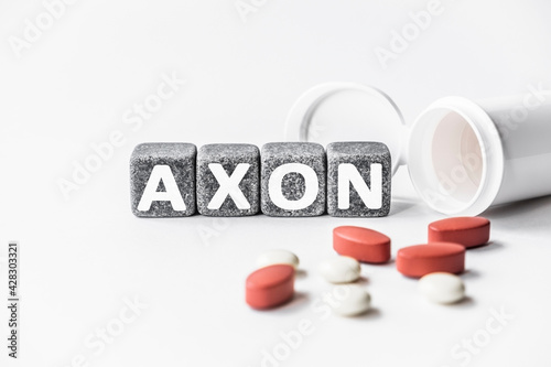 word AXON is made of stone cubes on a white background with pills. medical concept of treatment, prevention and side effects. extension of nerve cell, conducts electrical impulses photo