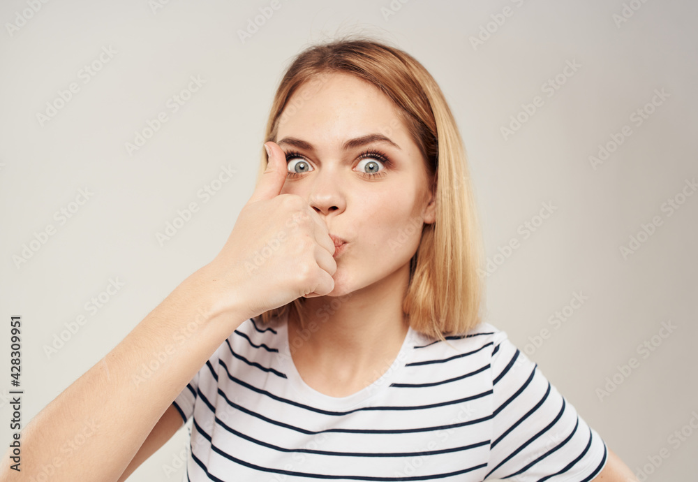 Cheerful blonde on a light background shows a finger and a cropped striped T-shirt can be seen Cheerful blonde on a light background shows a finger and a cropped striped T-shirt can be seen